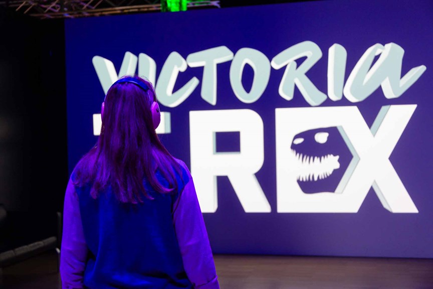 A person with headphones on looking at the sign to the Victoria the T. rex exhibition.