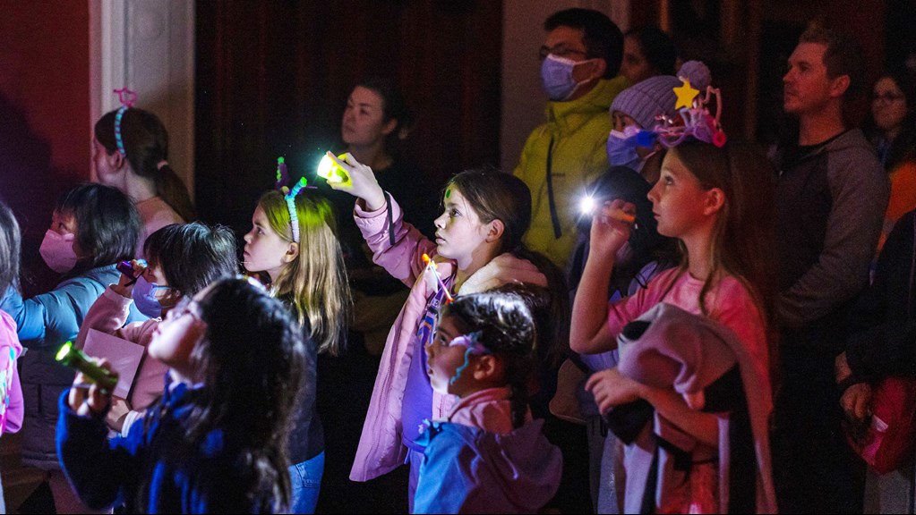 Children wearing colourful headbands made from pipe cleaners hold torches during a story time after dark event at the state library of victoria.