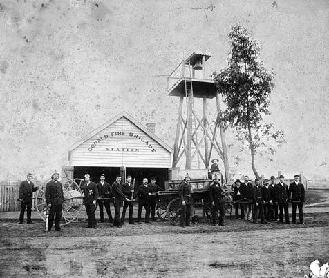Black and white image of a group of firemen with equipment outside a building