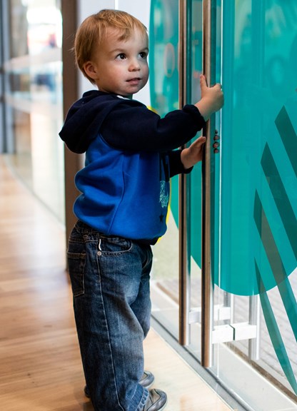 Toddler standing at the doors to the outdoor playground in the Children's Gallery