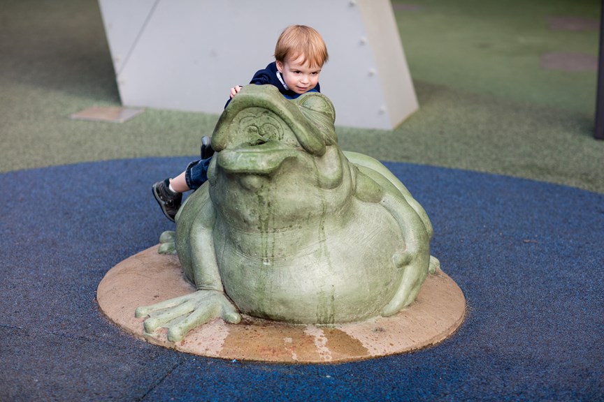 Child climbing on Tiddalik, the frog statue, in the water play area in the Children's Gallery outdoor playground