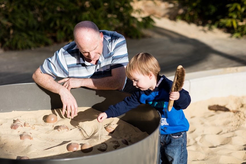 A man and a child uncovering fossils in the 'Dinosaur Dig' sandpit in the Children's Gallery outdoor playground
