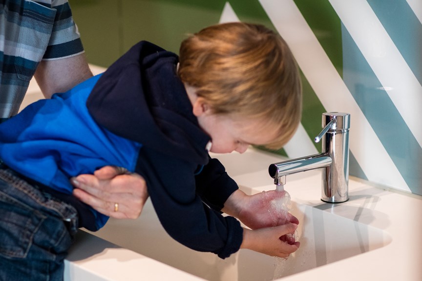 Toddler washing his hands at a sink in the family bathrooms at the Children's Gallery