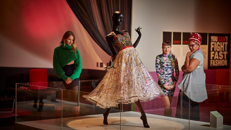 Three women looking at the Jenny Bannister 'Splash Plastic' dress on display in the 'You Can't Do That' exhibition at Melbourne Museum.