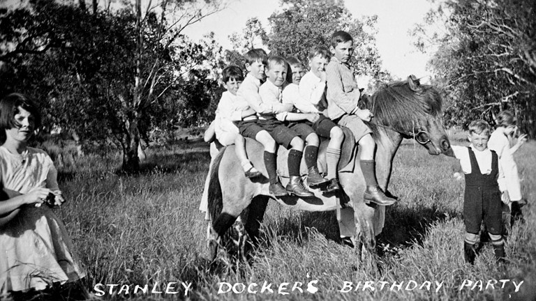 Six small boys on a horse. There is a girl on the left and a small boy on the right is holding the horse.