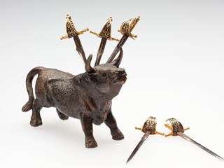 Metal bull with six holes in its neck into which slot five miniature swords.
