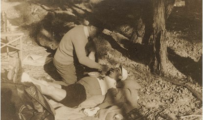 Man lying on ground being spoonfed by another man