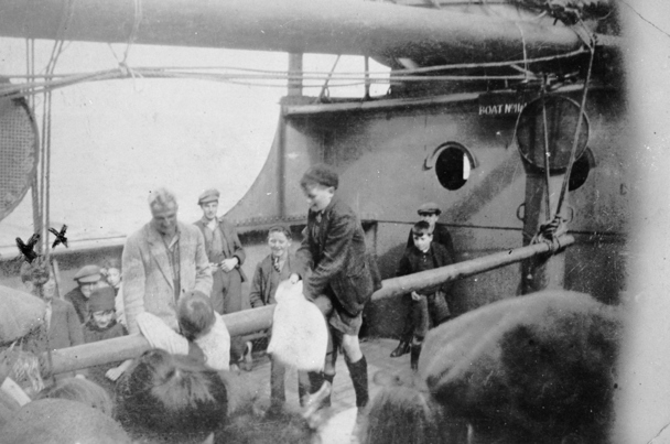 Small boys on a greasy pole on the SS Beltana. One boy is straddling the pole while another is leaning against it. There are two crosses marking the boy on the far left.