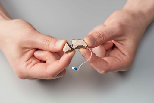 Two hands holding a hearing aid