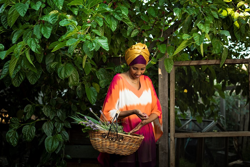 Mariam Issa holding a cane basket with produce in her garden 
