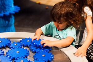 Child playing with blue cogs in the Ground Up exhibition 