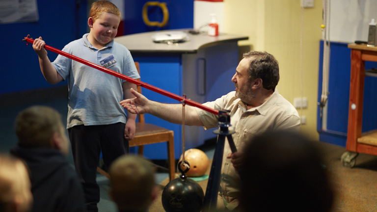 A boy in a school uniform is holding a leaver while a man is giving instructions