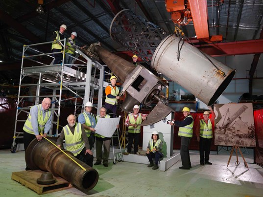 Workers in hi-vis next to a partially restored telescope.