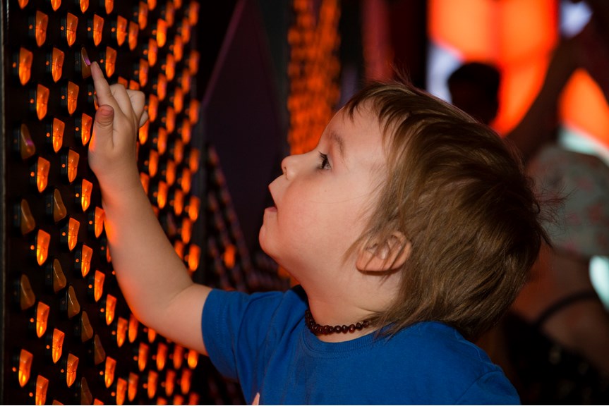 Boy touching the button switches on wall interactive in Ground Up exhibition at Scienceworks. 