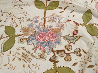 Appliqué quilt, with floral and bird pattern on heavy off-white fabric. Appliqué is made up of many different types of fabric, some printed with patterns such as flowers.