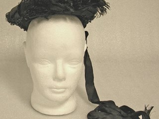 Black bonnet with net, sequins and a feather on a wire base.