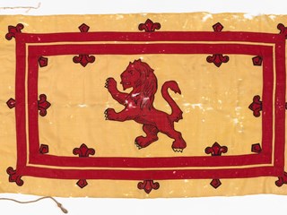 Flag: Scottish standard of the Caledonian Society, Minyip 1906 The standard shows a red lion, with a printed black outline against a yellow background. The lion is enclosed within a red rectangular border. Small red symbols with a printed black outline line the edges of the red border.