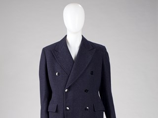 Dark blue, lined, double-breasted overcoat made of wool. Pockets on front at hip with flaps. Six black buttons on front; three black buttons at the cuff of each sleeve. 