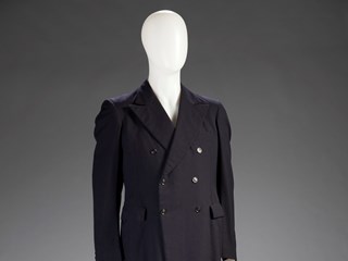 Three piece double breasted navy blue wool men's suit. The suit jacket has black lining, the navy trousers come with a set of crimson and blue striped braces, and the waistcoat has a white and blue striped lining and a black back. There is also a blue, red and yellow spotted handkerchief in the suit pocket.