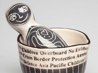 Glazed ceramic two piece artwork, consisting of a boat person in the shape of a mortar and pestle. Mortar contains text inspired by headlines relating to asylum seekers coming to Australia. Both pieces are glazed in black and white.