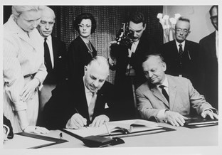 Hubert Opperman, seated, signing the German-Australian Migration Agreement, with several onlookers