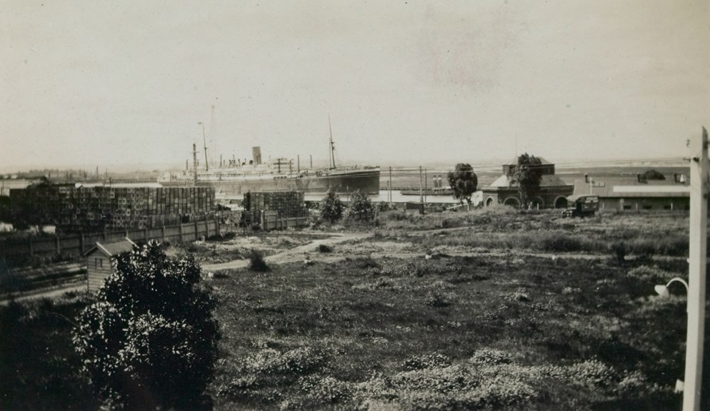 View from first floor balcony of Superintendent Engineer's residence at Spotswood Pumping Station, looking towards the north east showing glassworks storage yard, railway siding for delivery of coal to Pumping Station, roof of North Straining House and Corrugated Iron Workshop. In the background a large passenger steamship is moving down the Yarra River under towage by a steam tug. Note delivery van on arena track.