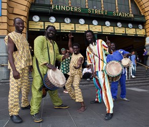 Group of men under the clocks at Flinders Street. Three are holding drums