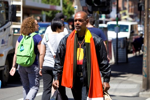 Man walking a long the street with an Aboriginal Flag draped over his shoulders