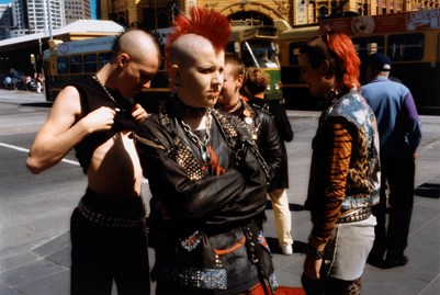 Group of people stand in the street. The person in the centre of the photograph has a red mohawk