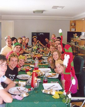 Extended family sitting around a Christmas table. Some are wearing paper hats.