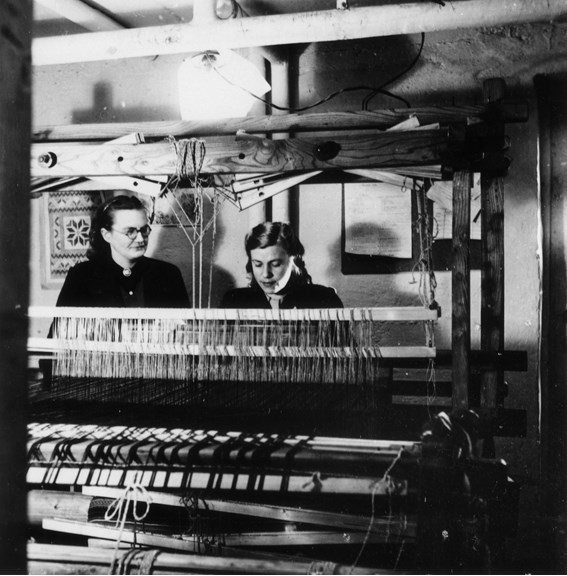 Black and white photograph of two women sitting at a weaving loom