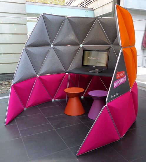 A colourful pod with a computer on a desk with two plastic stools
