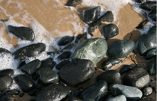 Greenish black pebbles on sand surrounded by foam from seawater