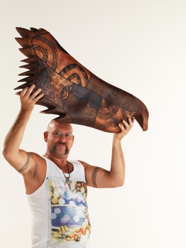 Artist Mick Harding holding aloft his wooden carving of Bunjil