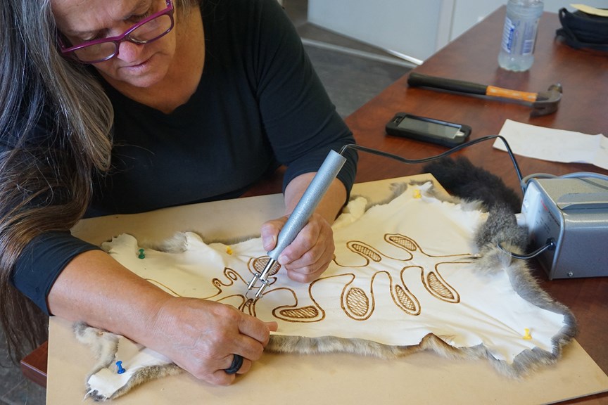 A woman sketches a design onto a possum skin with a wire-nib burner.