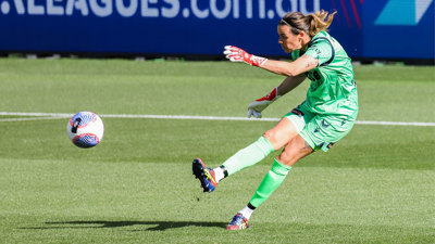 Goalkeeper Lydia Williams extending herself to kick a football away from the net.