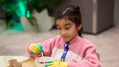 A young girl wearing gloves potting seeds while taking part in the Seed Stories workshop at Melbourne Museum.