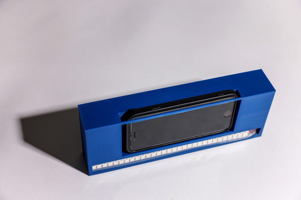 Blue rectangular device with a black phone holder slot in the centre and a strip of white LED lights along the bottom edge.