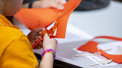 A child cutting orange paper with scissors during a crafting activity at Immigration Museum.