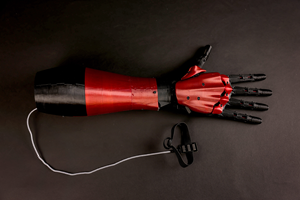 3D printed red and black prosthetic arm. A cable extends from the base of the arm, connecting to a sensor. 