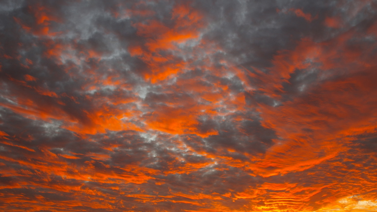 A bright orange and yellow sunset interspersed with grey clouds.