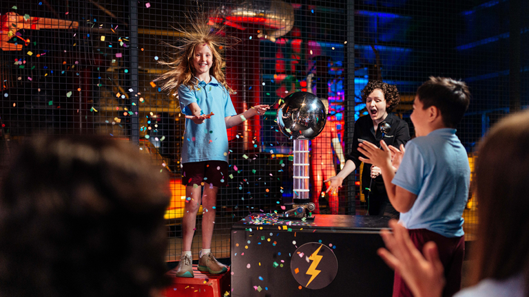 A child with long hair standing up caused by electricity from touching a Vandergraph at Scienceworks