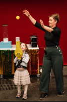 A child is holding a leaf blower and a ball is hovering above it in the air. Next to them is a show presenter.
