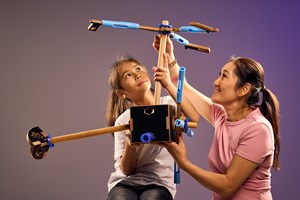 A girl and her mother hold up a helicopter constructed from wooden dowels and other loose parts in Tinkertown exhibition at Scienceworks.