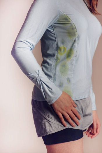 Side view of model wearing a pale blue, long-sleeved athletic top with gathered sleeve detailing and organic floral patterns in green and yellow tones, paired with grey running shorts and black bike pants.