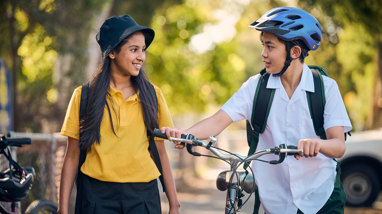 Two children walk their bikes down a sunny street sidewalk.