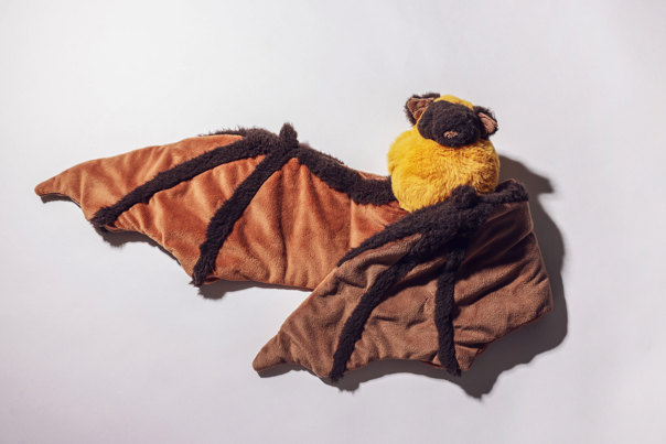 Plush bat toy with brown and tan striped wings, dark brown body, and yellow chest, displayed with its wings spread against a neutral background.
