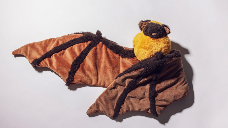 Plush bat toy with brown and tan striped wings, dark brown body, and yellow chest, displayed with its wings spread against a neutral background.