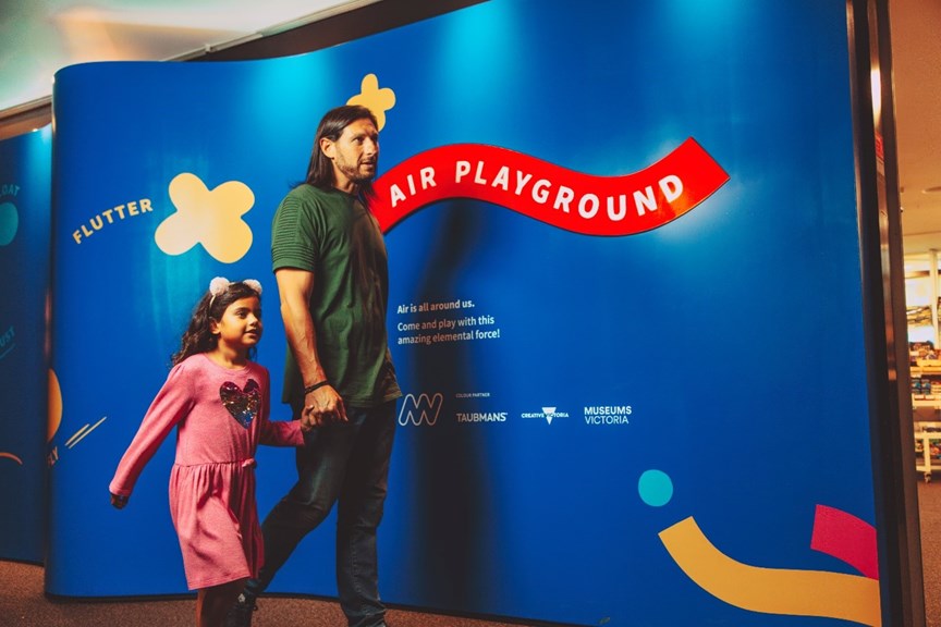 A girl holding her father's hand as they walk pass the Air Playground exit sign. 