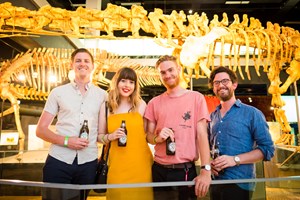 Four friends enjoying a beer in front of dinosaur skeletons in Dinosaur Walk.